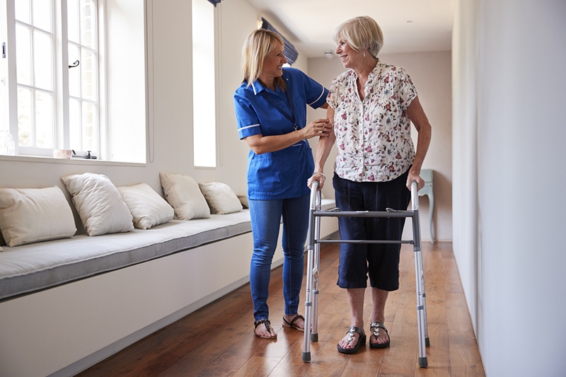 An older woman walking with a walker receiving help from a nurse at a long-term nursing care facility in Monroe, LA