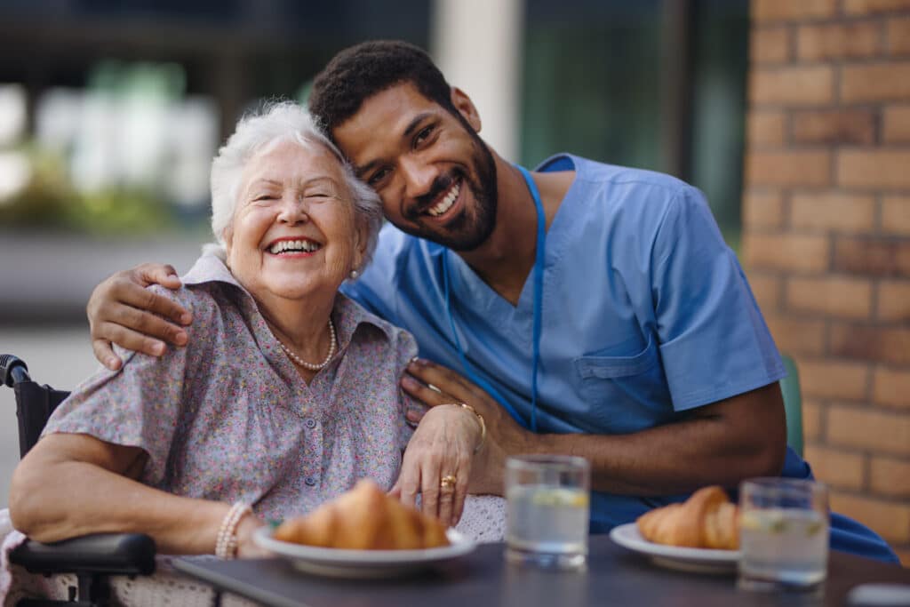 Elderly woman in wheelchair eating a meal with a nurse at assisted living in Monroe, LA